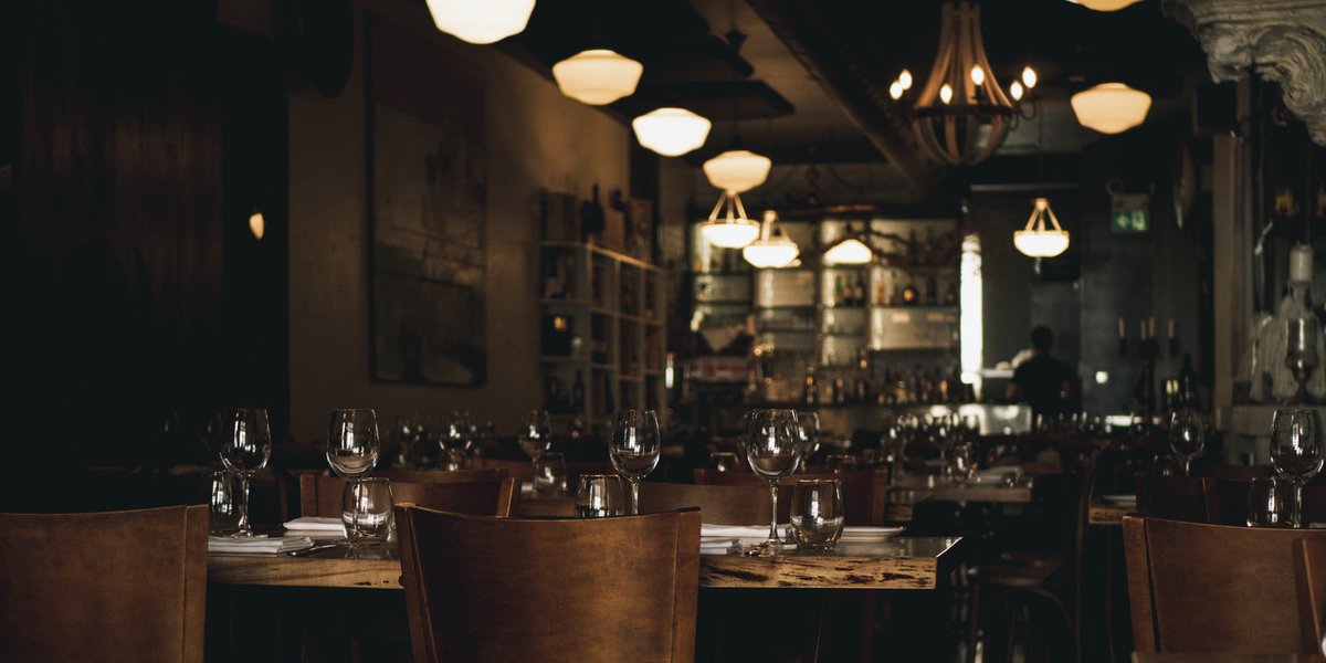 Salle de restaurant chaleureuse avec tables dressées, verres et suspensions lumineuses